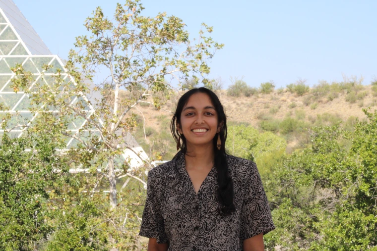 Person with long black hair, long wood earrings and brown short sleeve shirt smiling