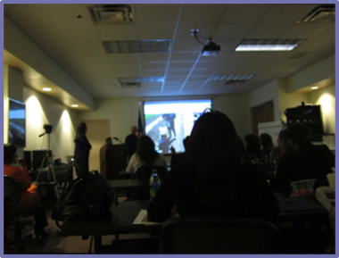 Foto de participantes mirando una pantalla que muestra una presentación